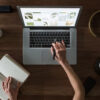 Person Using Macbook While Holding on Planner Book to Create a Website