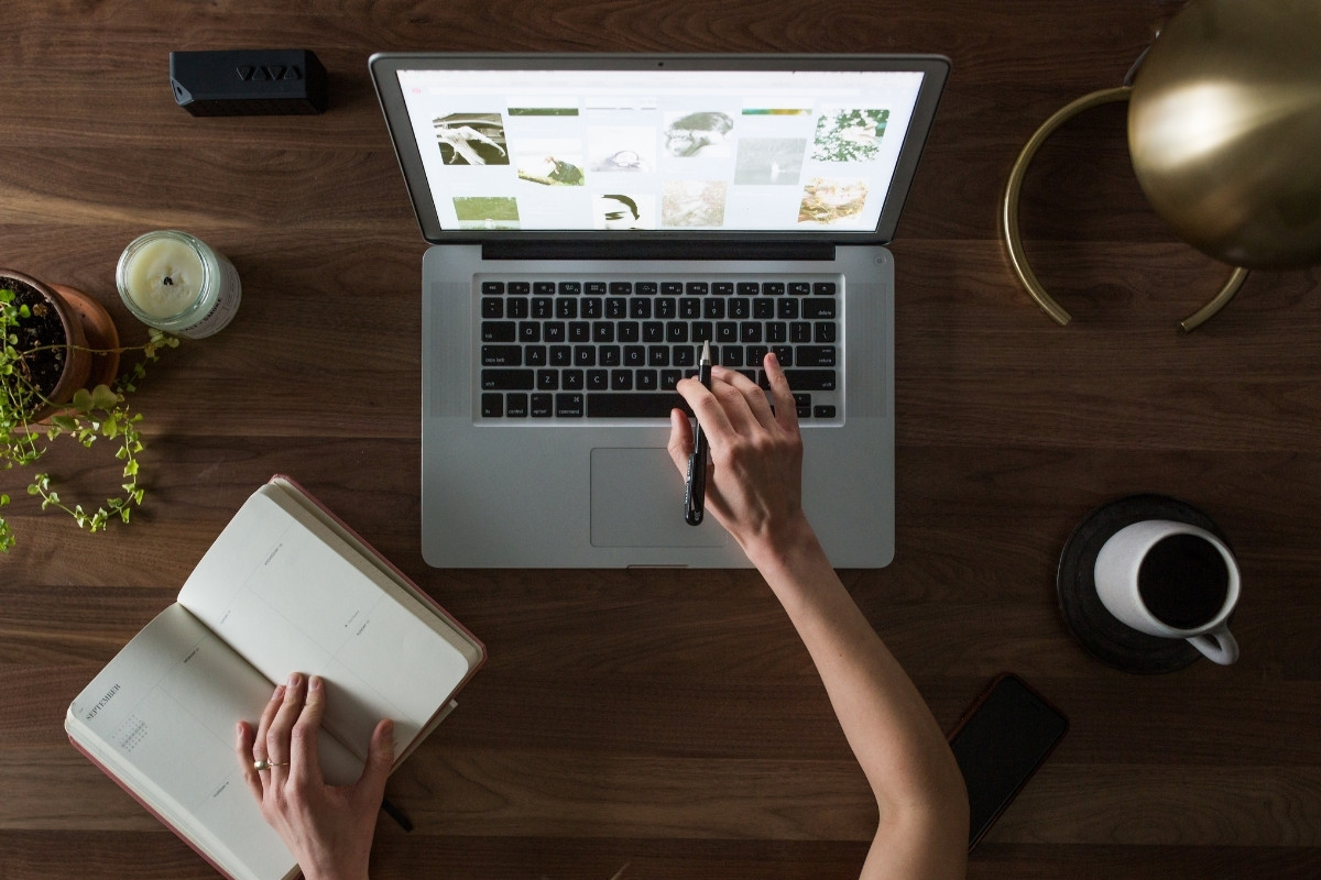 Person Using Macbook While Holding on Planner Book to Create a Website