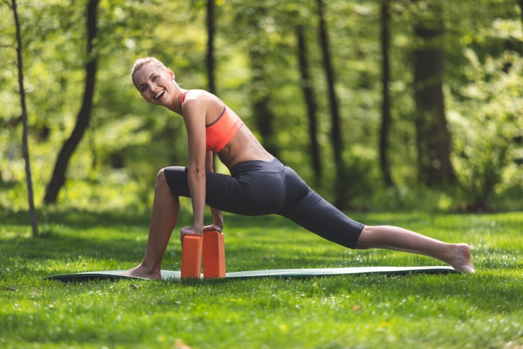 Grinning woman is training with yoga blocks outdoors