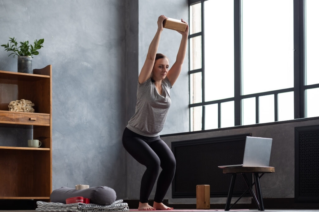 woman holding yoga block while in chair pose